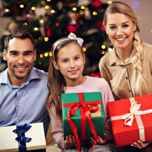 Father, daughter, mother in front of Christmas tree holding presents.