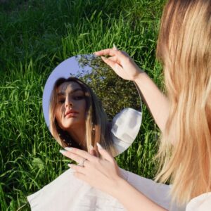 Woman sitting on grass looking in mirror.