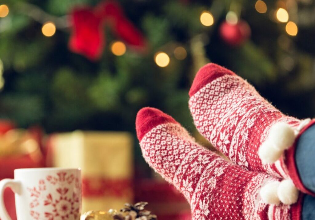 Christmas cup on table with someone's feet on the table with holidays socks on.