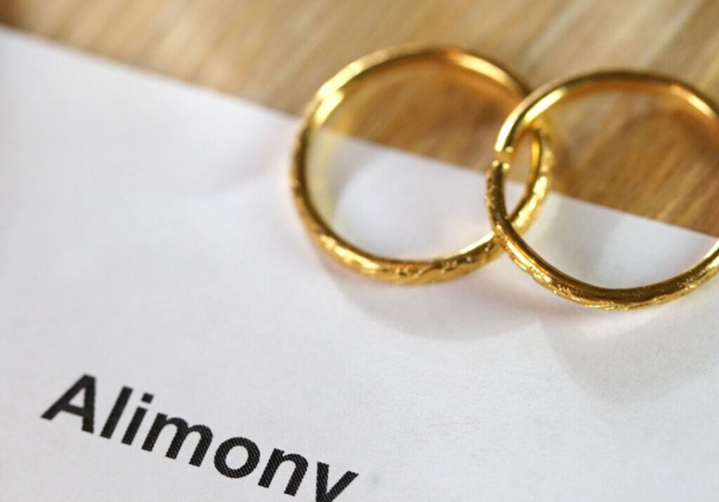 Alimony typed on paper with wedding rings laying on the paper.