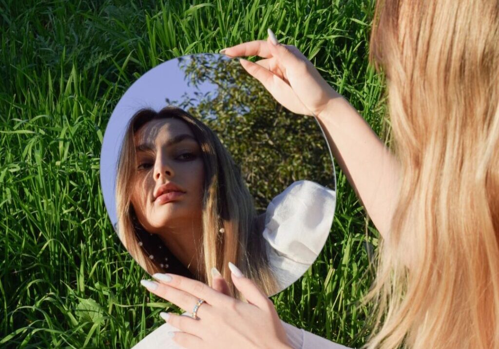 Woman sitting on grass looking in mirror.