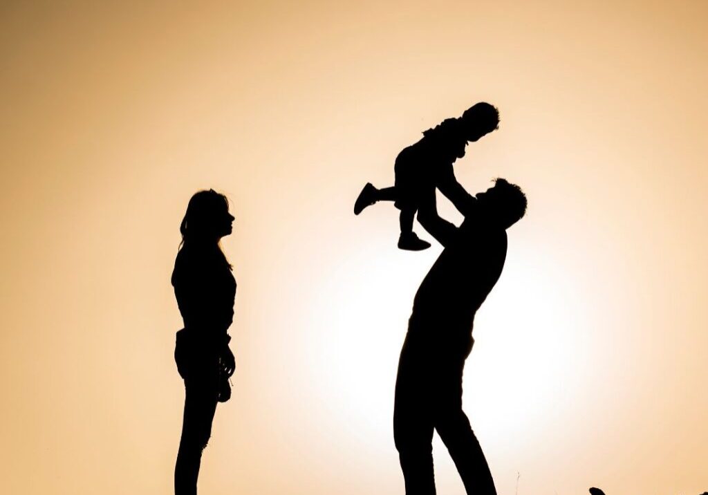 Father holding child up in the air while mother looks on.
